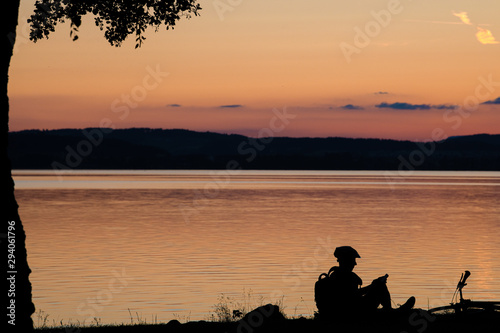 silhouette of bicyclist sitting at a lake during sunset after work