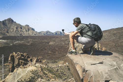 Travel blogger with backpack making video with action cam for social blog. Caucasian man taking pictures on a mountain cliff overlooking the lavic panorama. Holiday, travel, new trend tech concept. photo