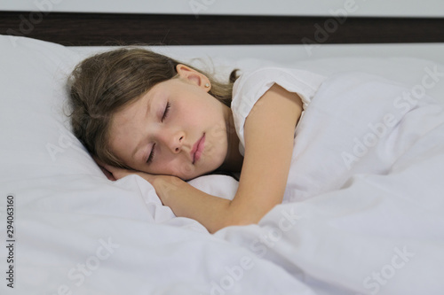 Sleeping child girl on a pillow, white bed, closeup face