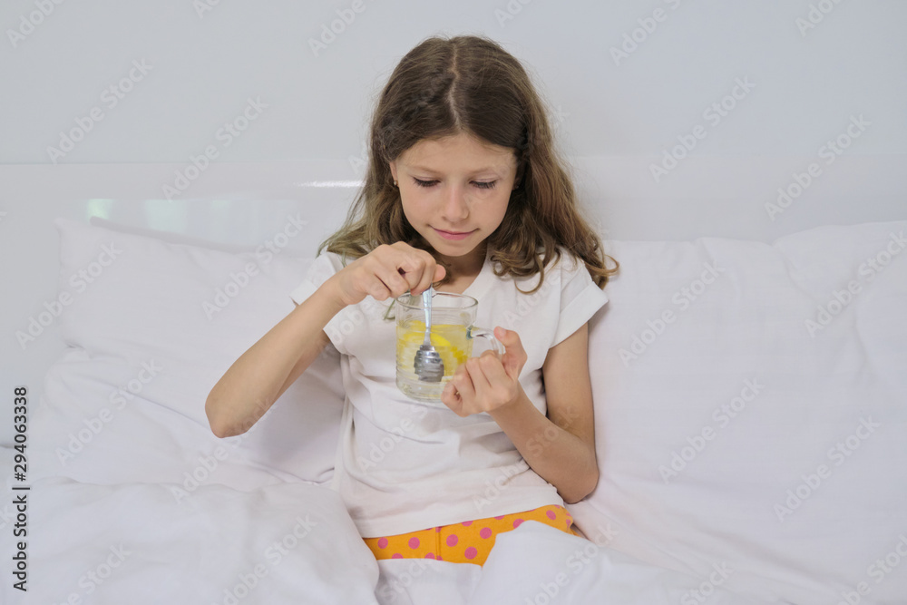 Smiling little girl holding a glass of natural homemade drink with lemon sitting in home white bed Smiling little girl holding a glass of natural homemade drink with lemon sitting in home white bed