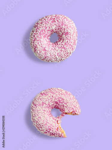 Two pink donuts on a purple background. One donut is whole and the other is bitten. Donuts with pink glaze and white sprinkles.