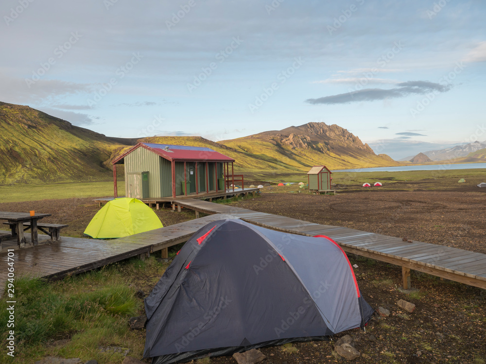 Colorful tents at camping site on blue Alftavatn lake with green hills and glacier in the otherwordly beautiful landscape of the Fjallabak Nature Reserve in the Highlands of Iceland part of famous