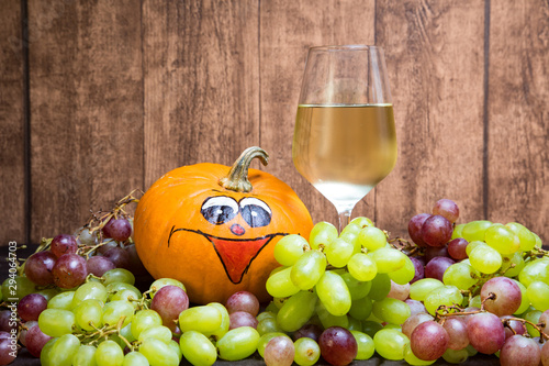 Glass of white wine with pumpkin and grapes during autumn. Iwith a natural wooden plate as the background.