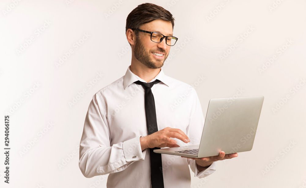 Cheerful Businessman Working On Laptop Standing In Studio, White Background Cheerful Businessman Working On Laptop Standing In Studio, White Background