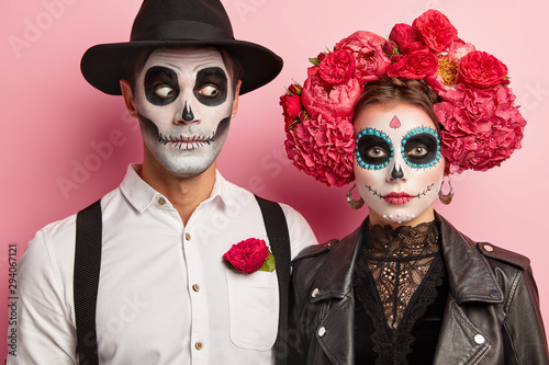 Halloween face art. Woman and man stand together in mexican outfit, spend time in cemetery, remember dead people during day of death, visit zombie party, express horror. Typical holiday in Mexico