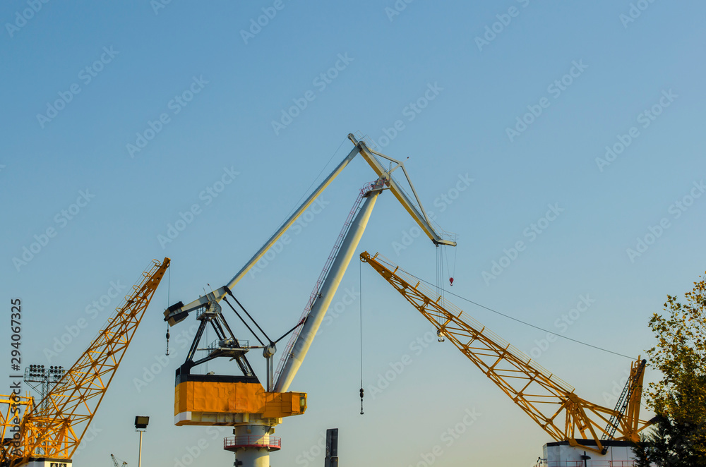 Yellow construction cranes close-up. Blue sky and white clouds. Place for text. Selective focus image. Copy space. Yellow construction cranes close-up. Blue sky and white clouds. Place for text. Selective focus image. Copy space.