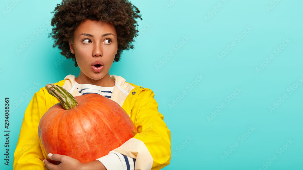 Photo of emotional shocked female with crisp hair, holds big orange