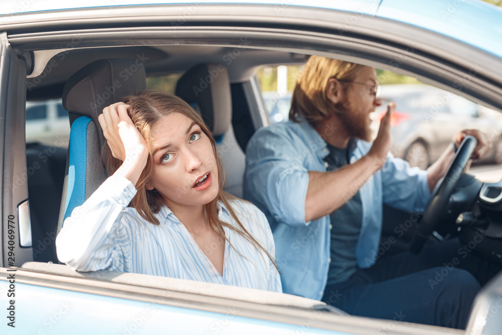 Angry young adult man and tired woman sitting in car