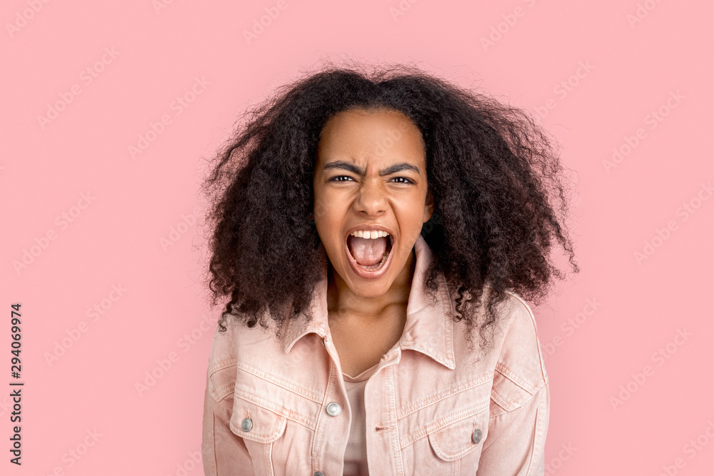 Freestyle. African girl in denim jacket standing isolated on pink screaming to camera angry
