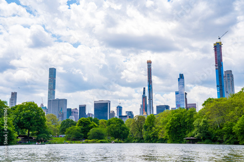New York City Manhattan skyline panorama viewed from Central Park with cloud and blue sky and people in lawn.