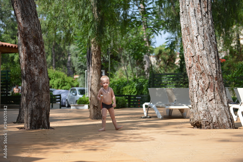 Fototapeta premium Young boy posing in summer park with palm trees. Cute spectacled happy teen boy 2 years old. Kid's outdoor portrait