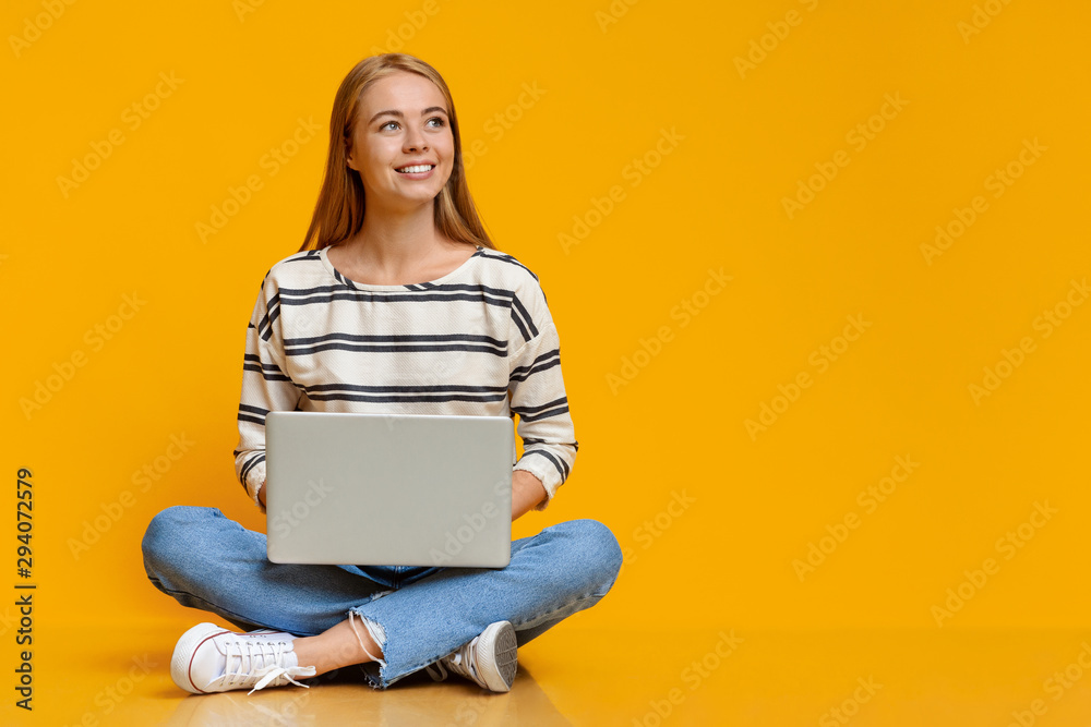 Teenage girl sitting with laptop on floor and looking aside Teenage girl sitting with laptop on floor and looking aside