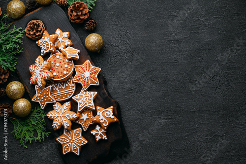 Christmas background with homemade gingerbread cookies, evergreen branches and decorations on black table. Festive food, New Year celebration traditions