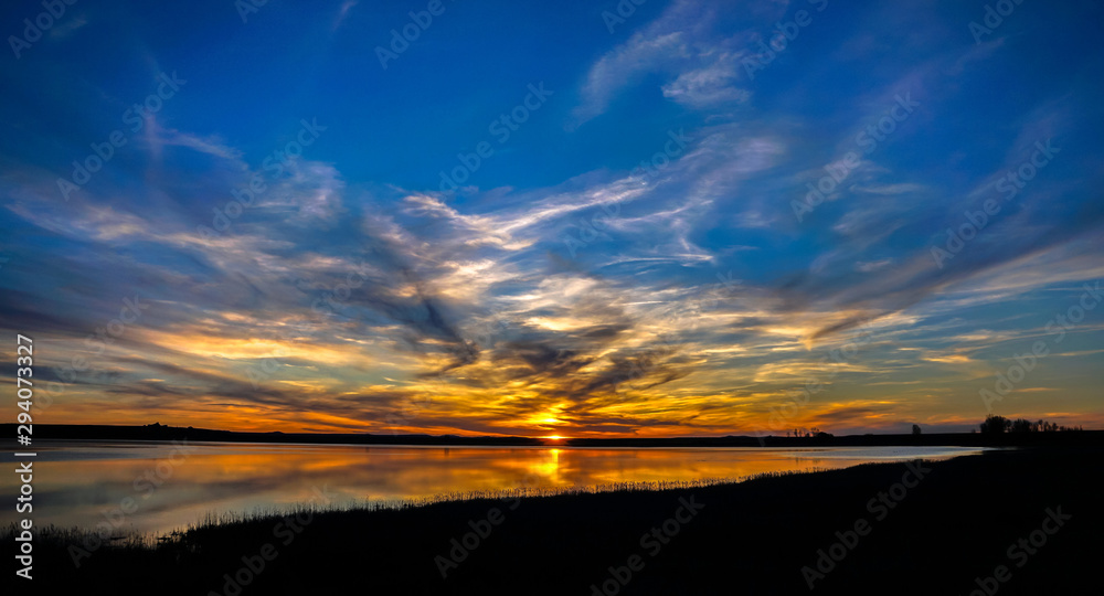 Colorful sunset sky with clouds over lake and reflection on water