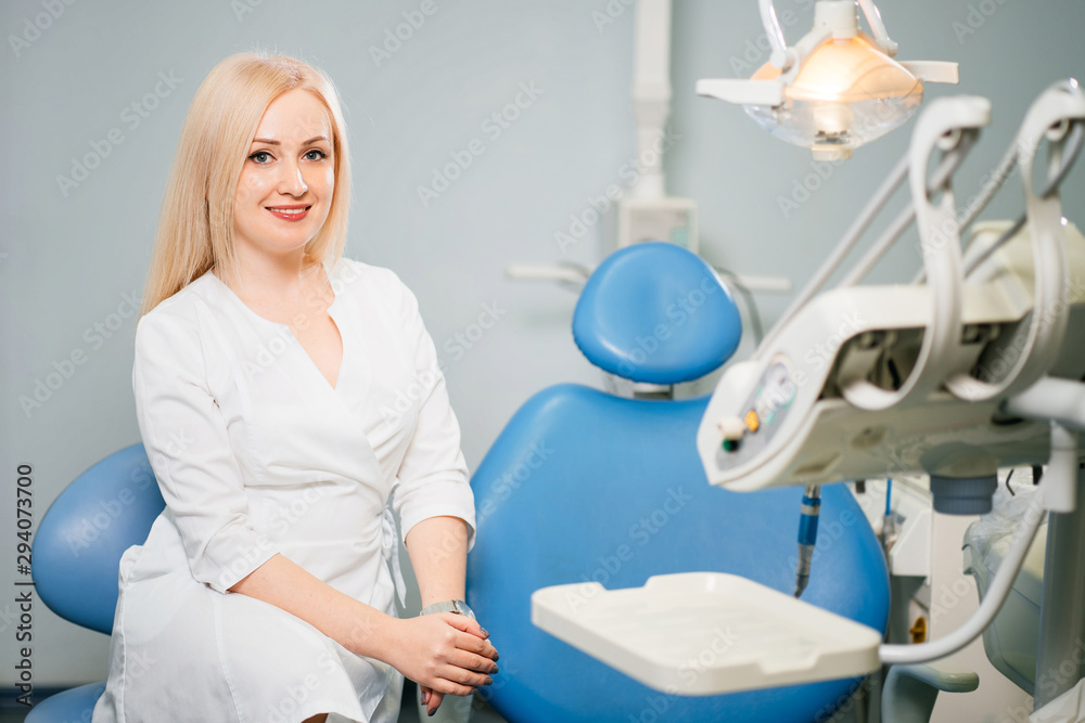 Dentistry, medicine, medical equipment and stomatology concept. Young woman dentist with dentist chair at the clinic. Dentistry, medicine, medical equipment and stomatology concept. Young woman dentist with dentist chair at the clinic.