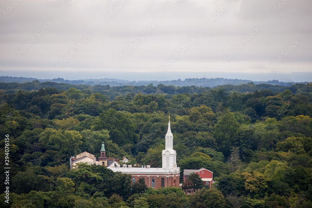White spire on brick building rises above sea of green trees