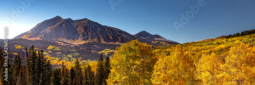 Panorama of a Rocky Mountain valley in Colorado with Aspen trees changing color in the fall season. The autumn colors are yellow, orange and a hint of red. 