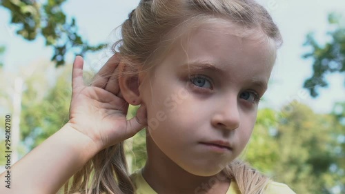 Cute caucasian girl holding hand near ear making listening gesture, gossip news