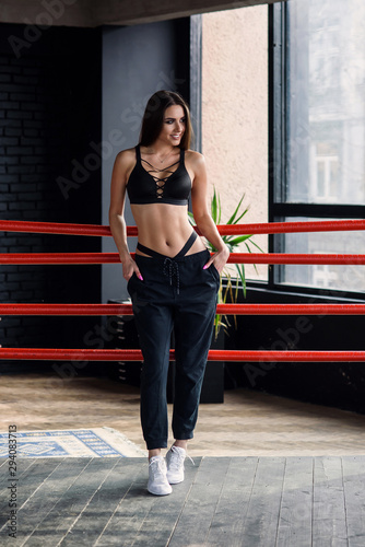 Sexy fitness girl in sportswear stands leaned on ropes of boxing ring.