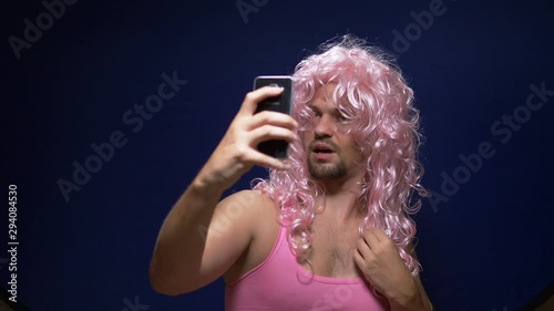 handsome crazy guy with a beard and in a pink wig makes sephi from a smartphone. dark background photo