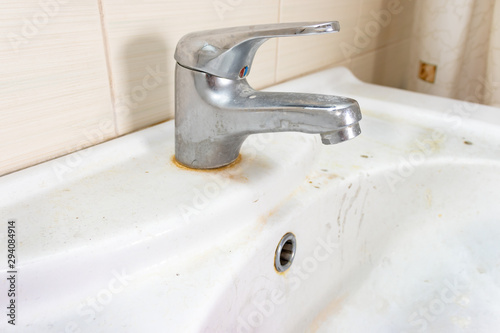 Old dirty washbasin with rust stains, limescale and soap stains in the bathroom with a faucet, water tap