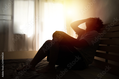 desperate man in silhouette sitting on the bed with hands on head , headache after weak up photo