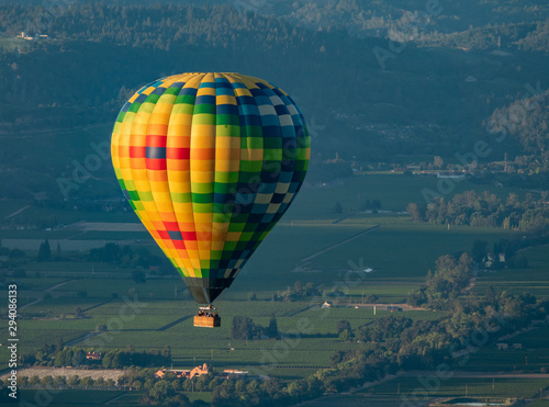A colorful hot air balloon flies high in the sky early in the morning at sunrise above the Napa Valley, California, known for its vineyards and wineries in addition to ballooning.   © David A Litman