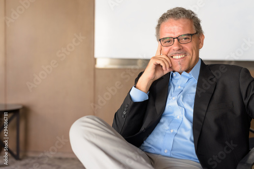 Happy mature Hispanic businessman smiling and sitting at the office