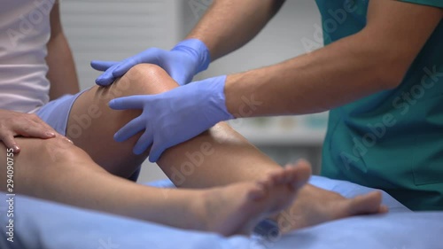 Doctor in gloves examining painful knee of female patient leg trauma, healthcare