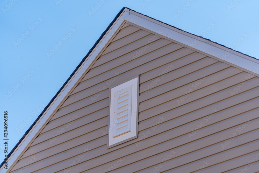 Gable with beige horizontal vinyl lap siding,  classic vertical surface mount PVC gable vent  on a pitched roof attic at an American single family home neighborhood USA
