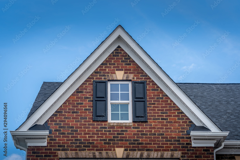 Gable with red brick facade siding, double hung window with white frame, vinyl shutters on a pitched roof attic at a luxury American single family home neighborhood USA