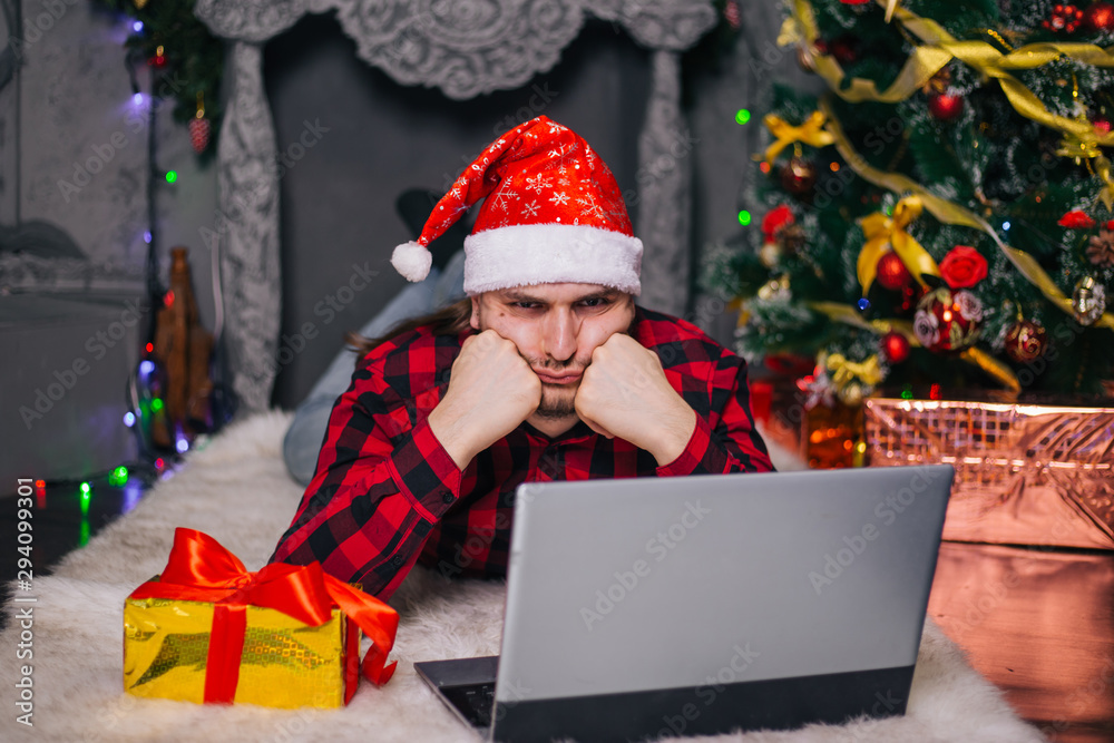 The guy in the red Santa hat is lying on the carpet near the fireplace. A man with a laptop. The guy in the red Santa hat is lying on the carpet near the fireplace. A man with a laptop.
