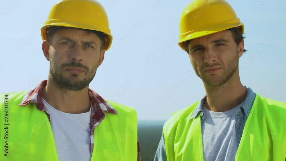 Professional builders in uniform and safety helmets seriously looking at camera Professional builders in uniform and safety helmets seriously looking at camera