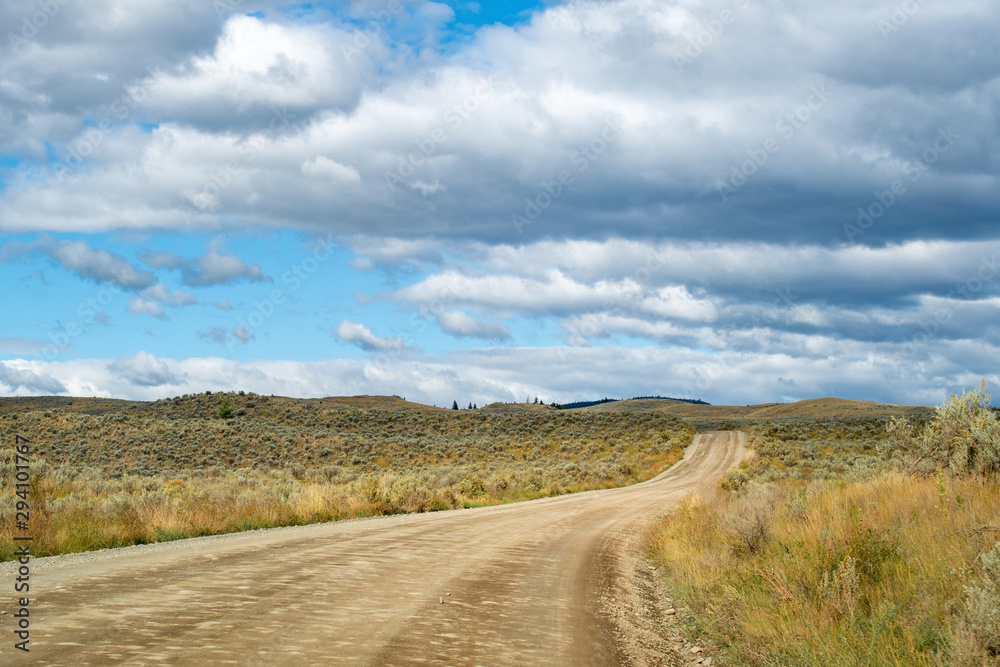 Winding dirt road among the hills with desert like landscape, grasslands and bush in Kamloops, British Columbia. Lac Du Bois