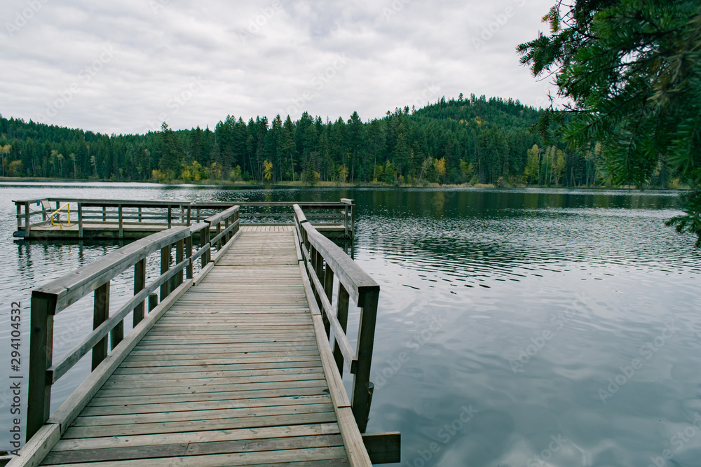 Dark green lakeside landscape with wooden dock pier, fall foliage forest, windy day, lake getaway