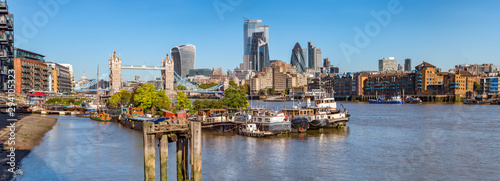 Panorama view of the Tower bridge over Thames river on a sunny day with wharf and boats. City Financial district skyscrapers and Tower of London in the background.