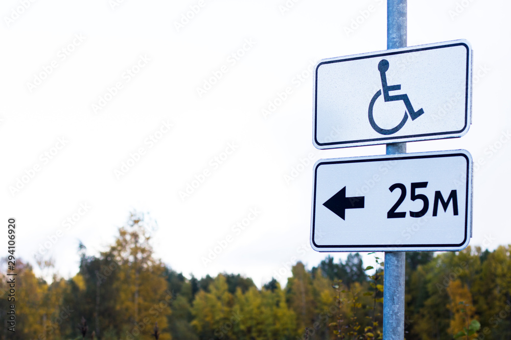 Road sign. Space on parking lot reserved for disabled invalid person, people with reduced mobility. Disability, handicapped parking sign. Autumn forest and sky background. Road sign. Space on parking lot reserved for disabled invalid person, people with reduced mobility. Disability, handicapped parking sign. Autumn forest and sky background.