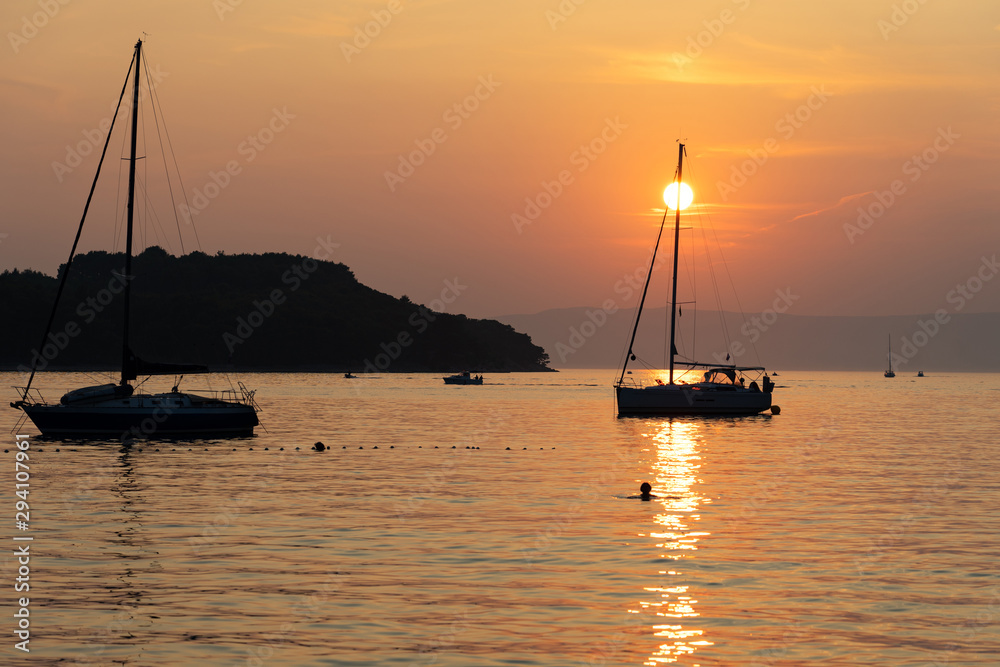 sunset on the sea with sailboats and islad silhouette
