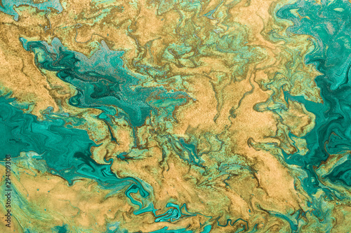 Acrylic fluid art. Abstract golden waves on green background with golden inclusions. Free flowing paint