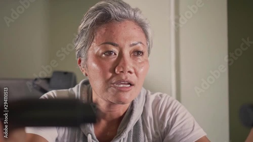 gimbal static bicycle shot on middle aged attractive and sweaty Asian Indonesian woman with grey hair training hard sweating at gym doing stationary bike workout in fitness concept