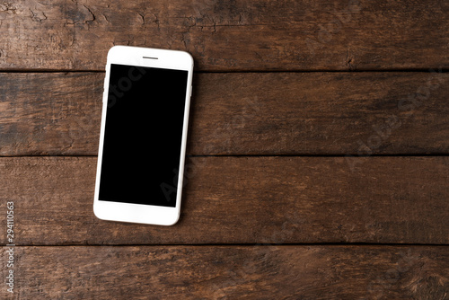 Mobile phone with empty screen on wooden desktop. Top view