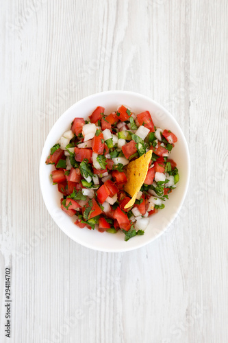 Pico de Gallo in a white bowl on a white wooden background, top view. Overhead, from above, flat lay.