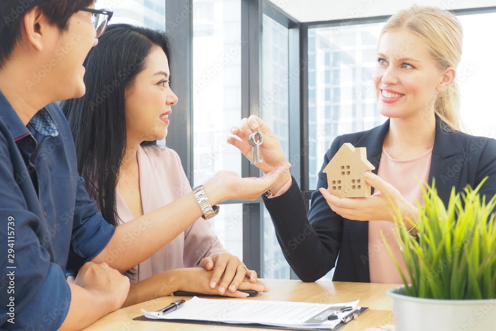 Professional female agent giving a house model and keys to couple after they decide to buy a new property in the real estate office. Home loan information also provided. Successful business concept Professional female agent giving a house model and keys to couple after they decide to buy a new property in the real estate office. Home loan information also provided. Successful business concept