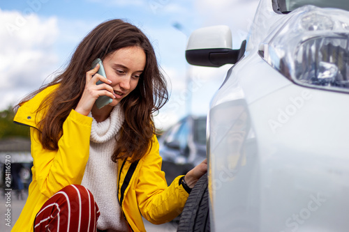 Upset woman talking on the phone near a broken car. Punctured car tire. Evacuator challenge. photo