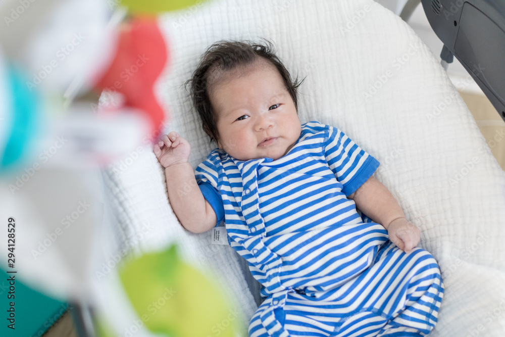 Obraz premium Cute baby laying in bouncer chair and looking mobile