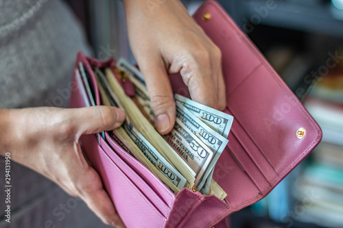 Woman taking out US dollar bills from her pocket wallet (depth of field photography).