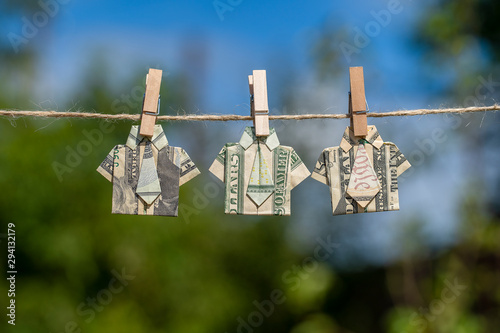 Origami shirt made of dollar banknote on hanging green nature background. Dollar bills hanging on a rope. Close up