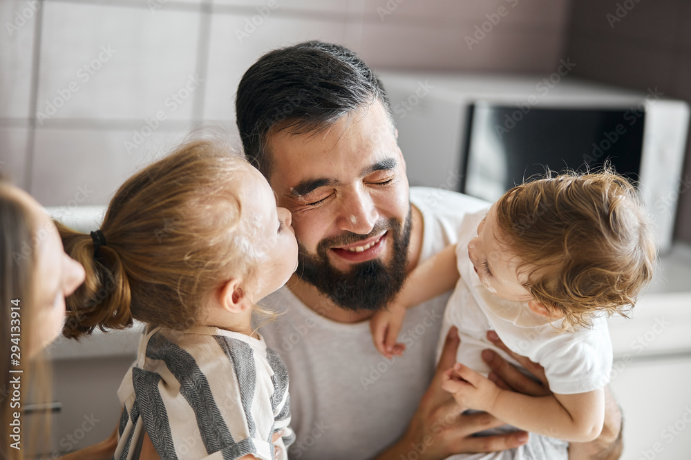 two adorable daughters kissing their daddy in the kitchen. close up photo. warm, tender feeling and emotion
