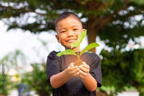 Soft focus. Happy Asian child boy hands holding a little green plant with soil. Growing tree. Spring season.