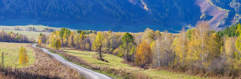 Autumn road, scenic panoramic view. Yellow trees on a background of blue mountainside.